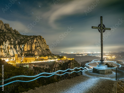 Paisaje nocturno de la montaña de Montserrat con fondo iluminado de poblaciones en Cataluña (España).