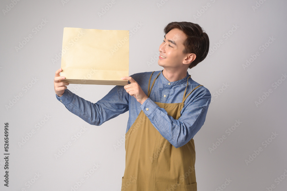 Portrait of young asian man wearing apron holding paper bag over white background studio, Save earth concept. Portrait of young asian man wearing apron holding paper bag over white background studio, Save earth concept.