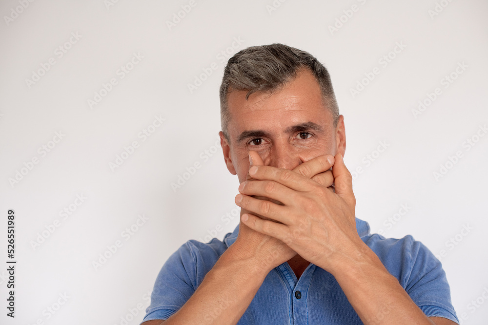 Portrait of mature man wearing blue T-shirt covering mouth. Caucasian man standing and looking at camera against white background unable to speak. Speak no evil concept Portrait of mature man wearing blue T-shirt covering mouth. Caucasian man standing and looking at camera against white background unable to speak. Speak no evil concept