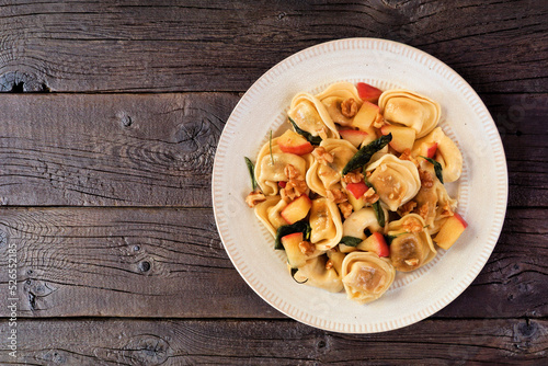 Pumpkin and apple tortellini pasta with walnuts and brown butter sage sauce. Top down view on a dark rustic wood background.