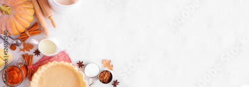 Fall baking corner border with pumpkin pie ingredients. Above view over a white marble banner background with copy space.