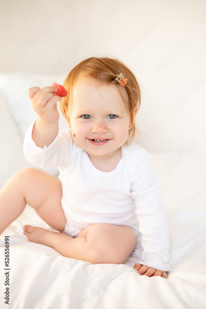 A cute red-haired baby girl eats raspberries, drinks water. Children's food. Light background. Space for text. Lifestyle A cute red-haired baby girl eats raspberries, drinks water. Children's food. Light background. Space for text. Lifestyle