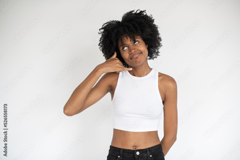 Portrait of pensive African American woman making phone gesture. Young female model wearing white crop top and jeans standing with thoughtful expression. Contact us concept