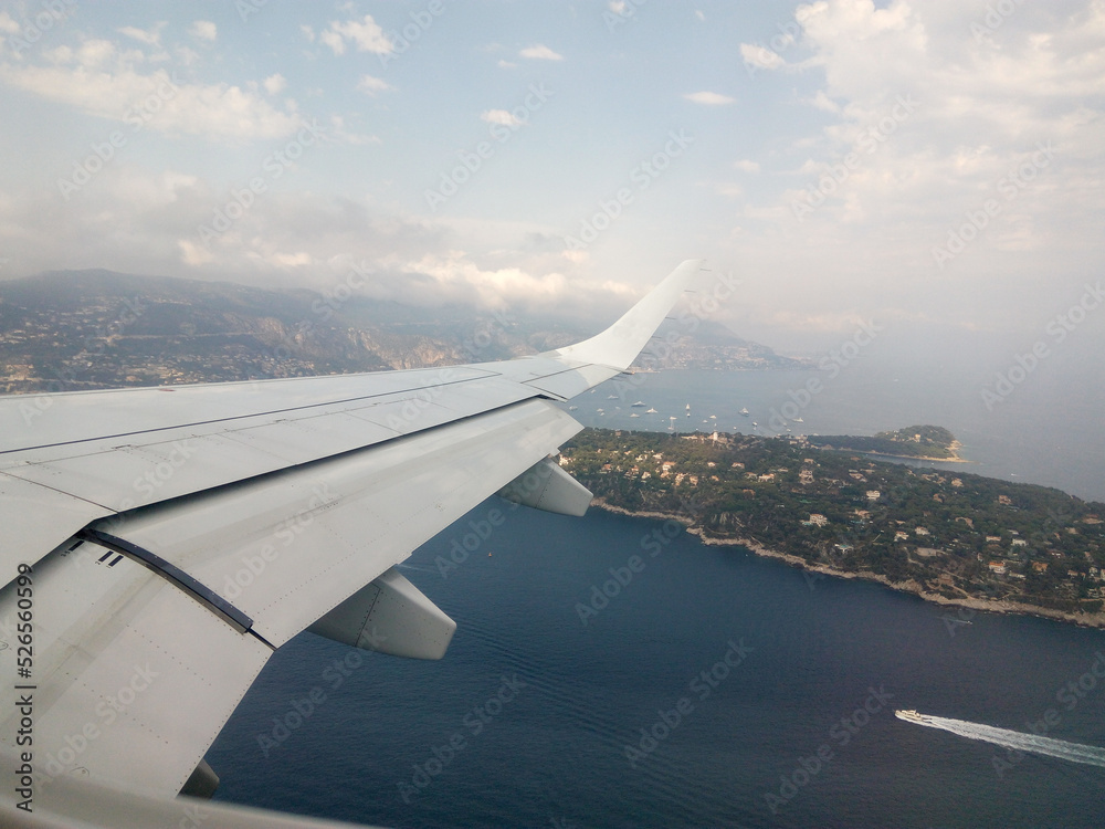 Scenic panoramic view of the city from the plane window. Natural beauty of blue sky with clouds. Wing of the aircraft on a cloudy day. Airplane flight and landing at the airport in Nice, France.