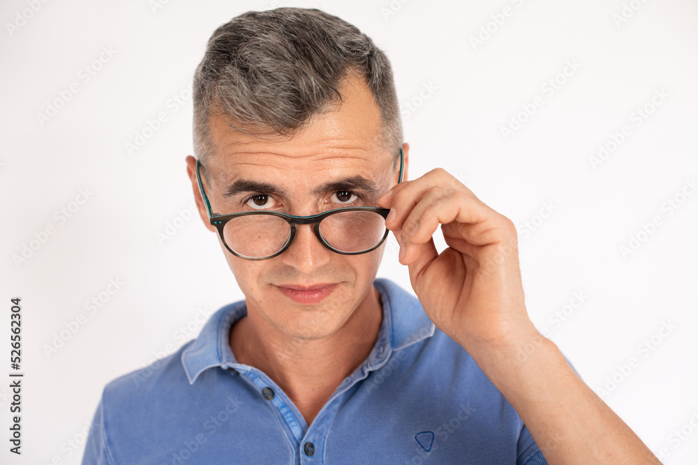 Portrait of serious mature man looking over spectacles. Caucasian man wearing blue T-shirt standing over white background. Eyesight concept Portrait of serious mature man looking over spectacles. Caucasian man wearing blue T-shirt standing over white background. Eyesight concept