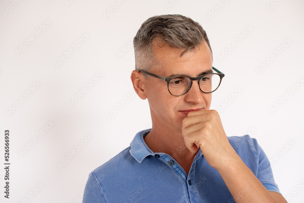 Portrait of pensive mature man wearing glasses with hand on chin. Caucasian man wearing blue T-shirt standing and thinking against white background. Solution concept Portrait of pensive mature man wearing glasses with hand on chin. Caucasian man wearing blue T-shirt standing and thinking against white background. Solution concept