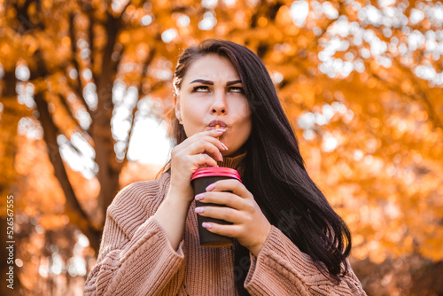 Pregnant woman standing in autumn city park forest  drinking hot beverage coffee tea  making faces grimaces. Fall time  red orange and yellow leaves. Mother s love  pregnancy concept 