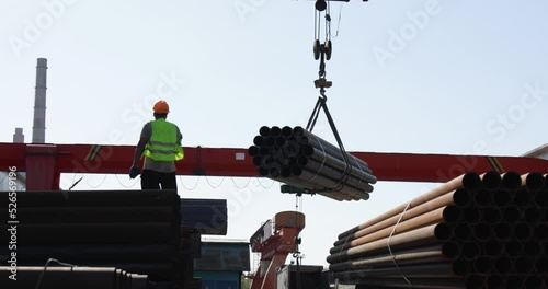 Worker transporting stack of metal pipes with gantry crane photo