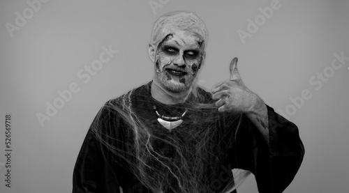 Sinister man with scary Halloween zombie makeup in costume raises thumbs up agrees with something or gives positive reply recommends advertisement likes good. Dead guy with wounded bloody scars face