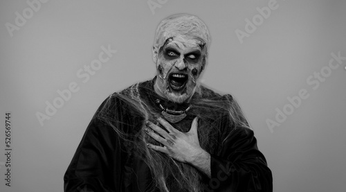 Sinister man in carnival costume of Halloween crazy zombie with bloody wounded scars face pointing finger to camera, laughing out loud, taunting making fun of ridiculous appearance, funny joke. Horror