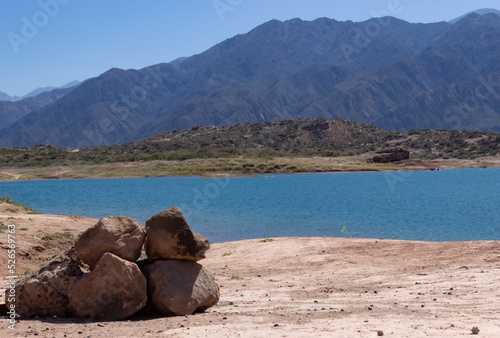 Stones by a lake in a beautiful scenery with mountains on a sunny day.