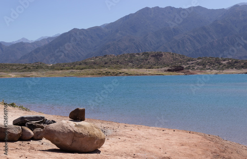 Stones by a lake in a beautiful scenery with mountains on a sunny day.
