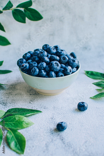 Ripe blueberry in  bowl with green leaves over gray table background copy space.