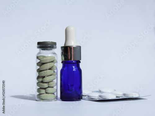 Closed glass jar with green pharmaceutical pills, a blue pipette with healthcare drops and white antibiotics on a white background