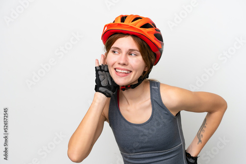 Young cyclist English woman isolated on white background listening to something by putting hand on the ear