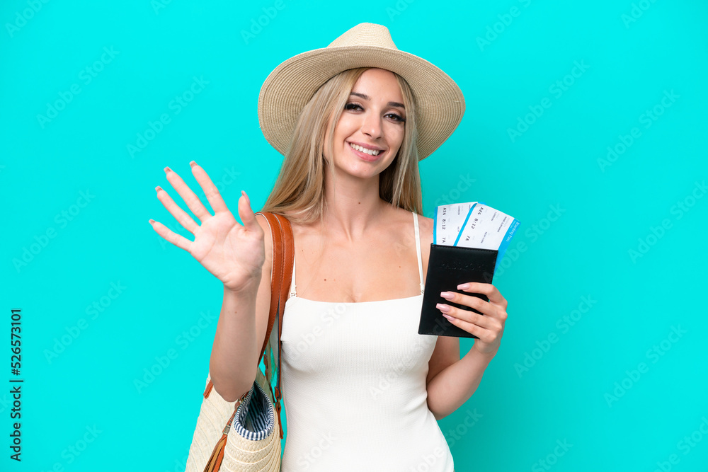 Blonde woman in swimsuit holding passport isolated on blue background saluting with hand with happy expression Blonde woman in swimsuit holding passport isolated on blue background saluting with hand with happy expression