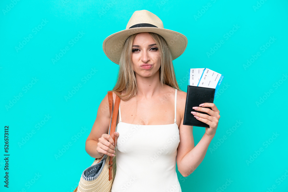 Blonde woman in swimsuit holding passport isolated on blue background with sad expression Blonde woman in swimsuit holding passport isolated on blue background with sad expression