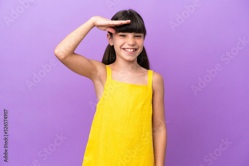 Little caucasian kid isolated on purple background saluting with hand with happy expression