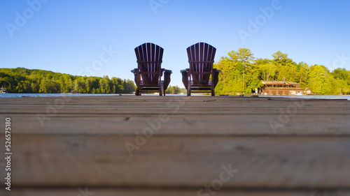 Two empty Adirondack chairs sitting on a dock on a lake in Muskoka, Ontario Canada. Calm morning on a cottege pier.