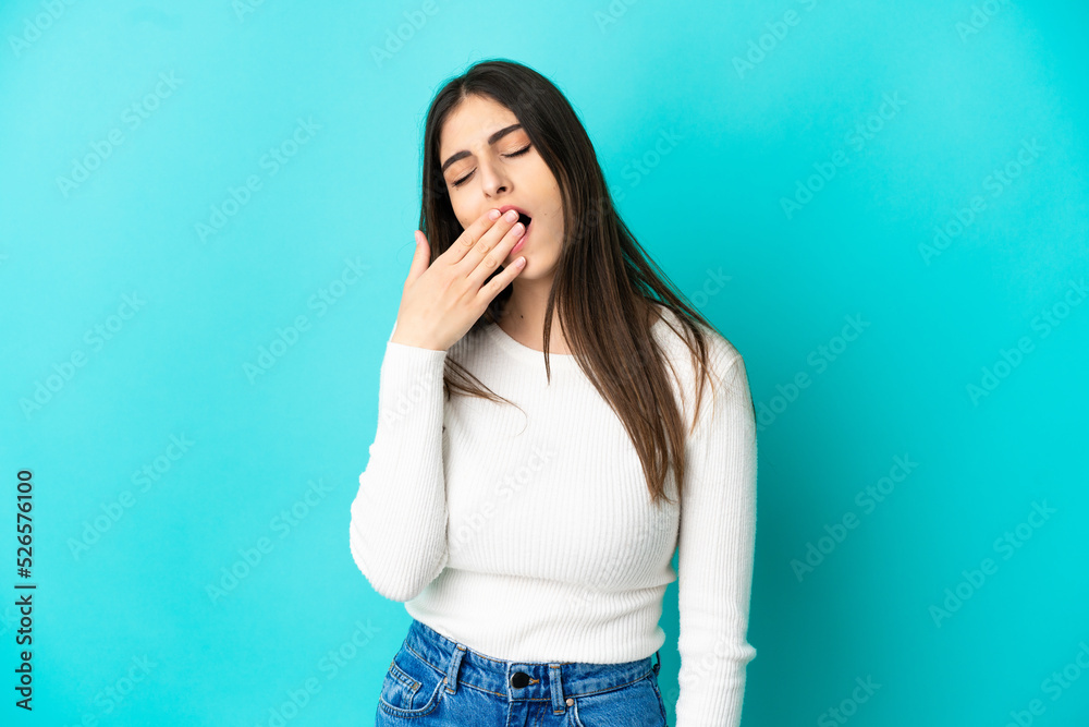 Young caucasian woman isolated on blue background yawning and covering wide open mouth with hand Young caucasian woman isolated on blue background yawning and covering wide open mouth with hand