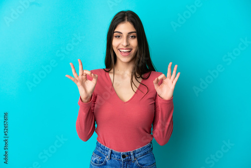 Young caucasian woman isolated on blue background showing ok sign with two hands