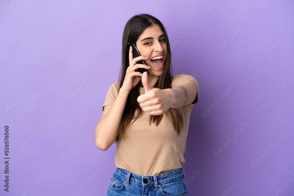Young caucasian woman using mobile phone isolated on purple background with thumbs up because something good has happened