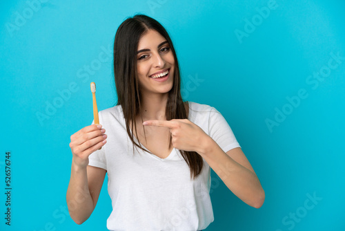 Young caucasian woman brushing teeth isolated on blue background and pointing it