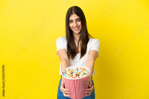 Young caucasian woman isolated on yellow background holding a big bucket of popcorns
