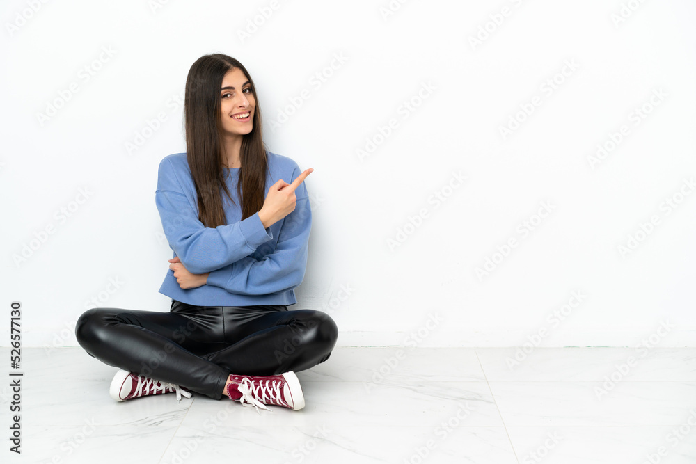 Young woman sitting on the floor isolated on white background pointing to the side to present a product Young woman sitting on the floor isolated on white background pointing to the side to present a product