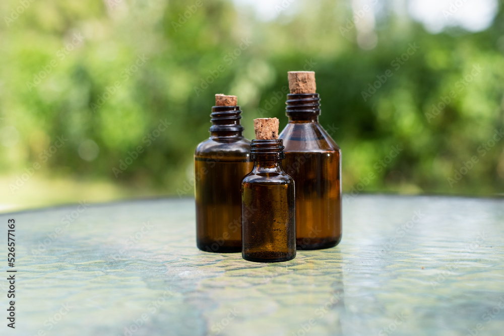 Small brown glass medicine bottles on glass table with green outdoor  background. Essential oil. 