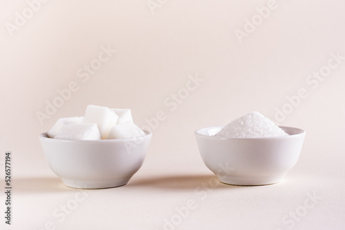 Sugar cubes and granulated sugar in bowls on a light background. Choosing between types of sugar