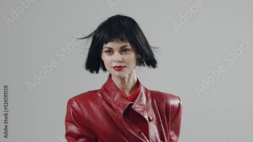 A young woman with beautiful bright make-up turns from her back looks at the camera and smiles with red painted lips on a light background. Fashion portrait woman