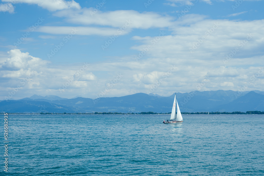 W boat with white sails on the bodensee in Switzerland. It is a sunny day with a blue sky. 