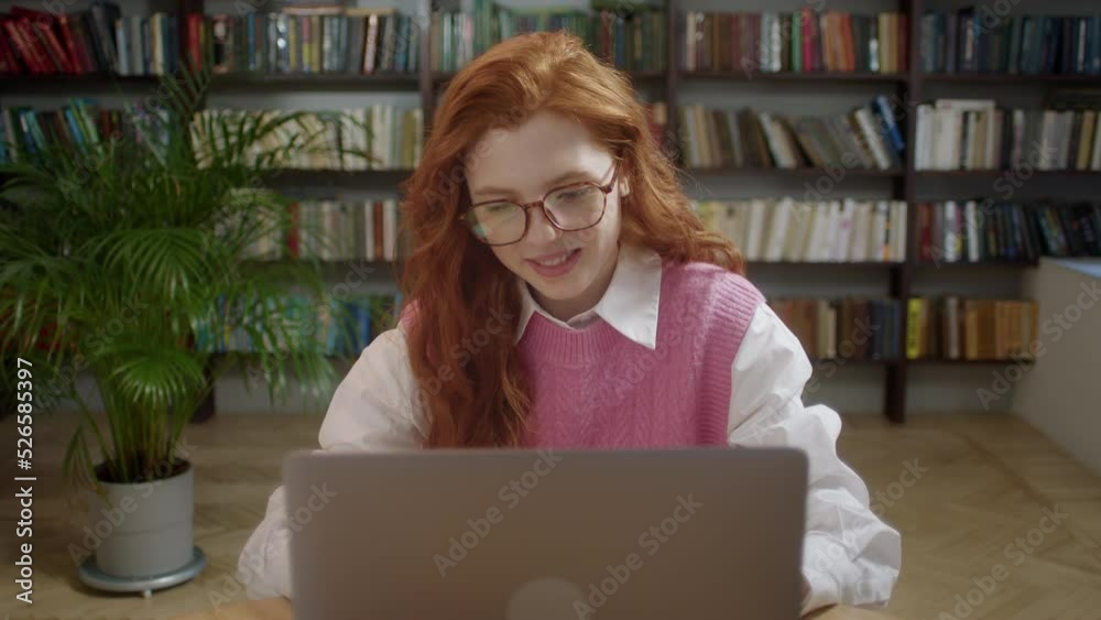 Focused Girl with red hair student using laptop search information internet course study online e learning in app typing on computer make notes write essay prepare for test exam sit at library desk