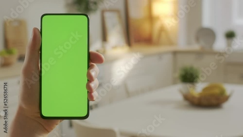 Handheld Camera: Point of View of Young Man at Home Sitting on Kitchen Room With Green Mock-up Screen Smartphone. Boy is Watcing Content Without Touching Gadget Screen. Modent Technology photo