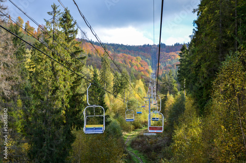 Empty aerial chair lift through colorful foliage in the autumn mountain forest 