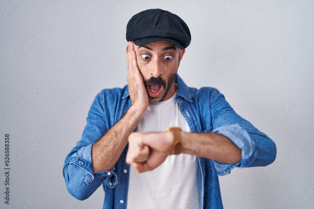 Hispanic man with beard standing over isolated background looking at the watch time worried, afraid of getting late