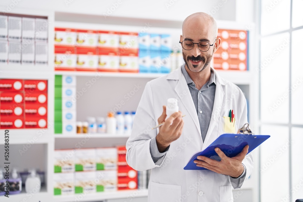 Young hispanic man pharmacist holding clipboard and pills at pharmacy