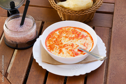 Bowl of traditional Balkan tripe soup, stew called Shkembe Chorba is made of tripe, cow or lamb stomach, wooden table, popular in Turkey and Macedonia, served with pickled garlic photo
