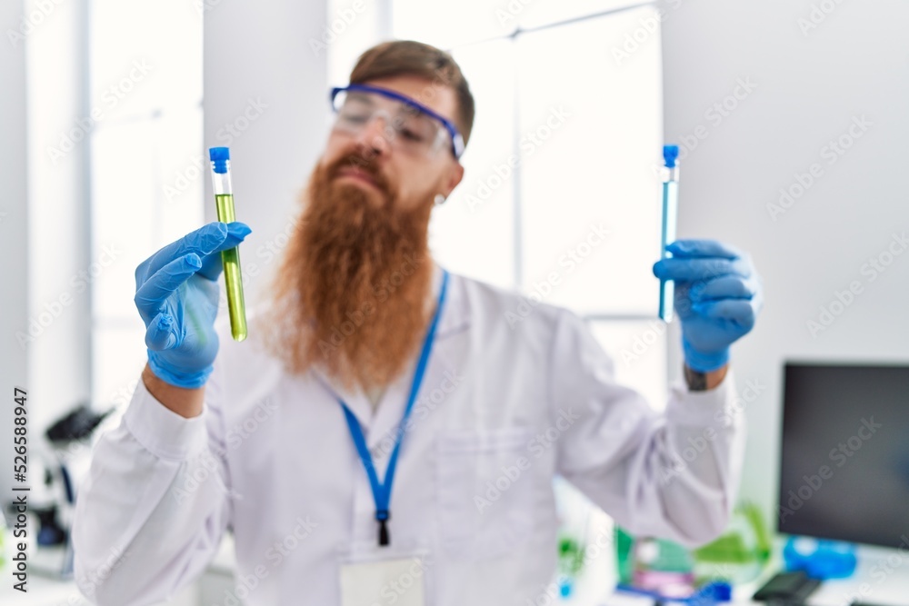 Young redhead man wearing scientist uniform holding test tubes at laboratory Young redhead man wearing scientist uniform holding test tubes at laboratory