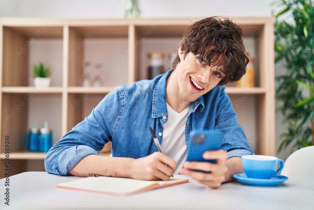Young hispanic man write on notebook using smartphone at home Young hispanic man write on notebook using smartphone at home