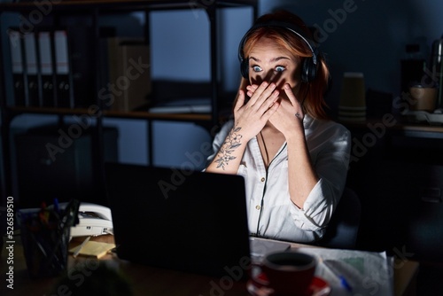 Young caucasian woman working at the office at night shocked covering mouth with hands for mistake. secret concept.