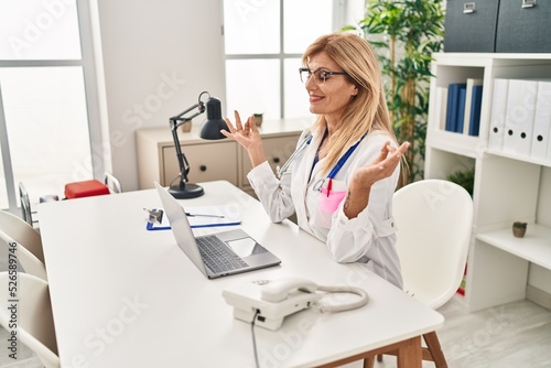 Middle age blonde woman wearing doctor uniform doing yoga exercise at clinic