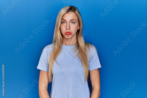 Beautiful blonde woman wearing casual t shirt over blue background depressed and worry for distress, crying angry and afraid. sad expression.