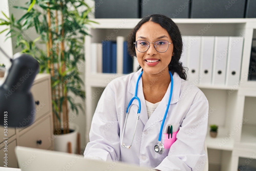 Young latin woman wearing doctor uniform using laptop working at clinic Young latin woman wearing doctor uniform using laptop working at clinic
