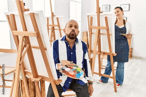 Senior artist man at art studio looking at the camera blowing a kiss on air being lovely and sexy. love expression.