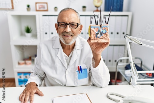Mature doctor man holding model of human anatomical skin and hair looking positive and happy standing and smiling with a confident smile showing teeth