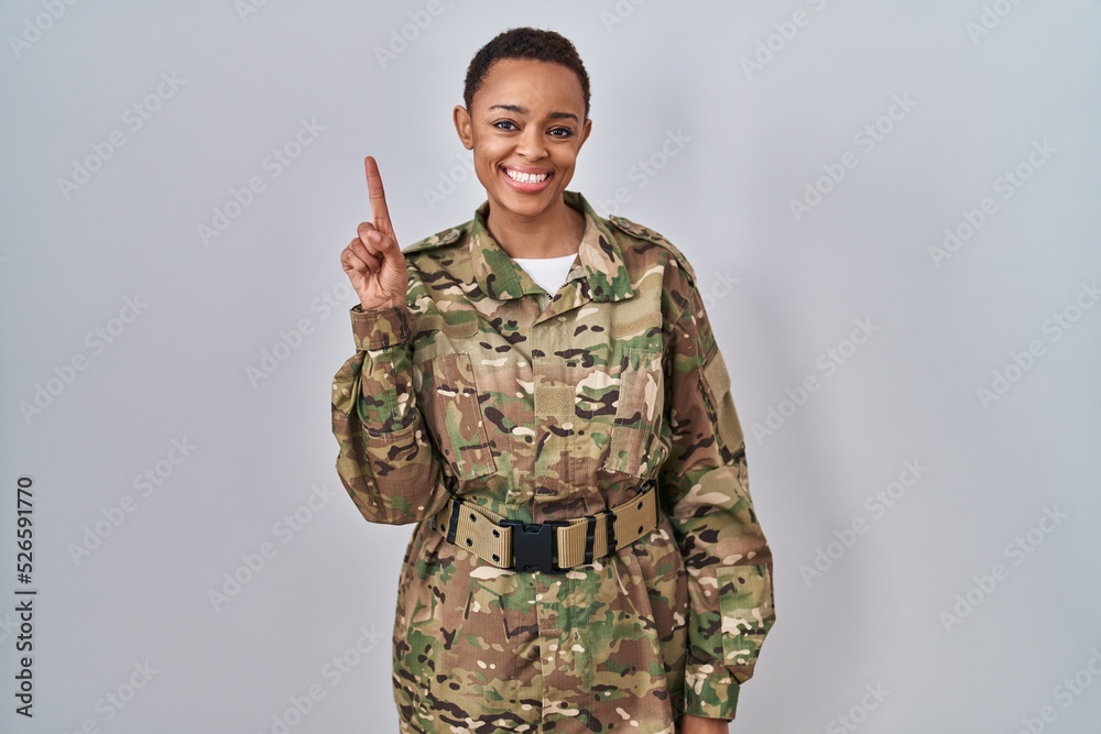 Beautiful african american woman wearing camouflage army uniform showing and pointing up with finger number one while smiling confident and happy. Beautiful african american woman wearing camouflage army uniform showing and pointing up with finger number one while smiling confident and happy.