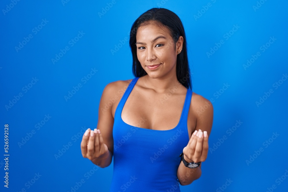 Hispanic woman standing over blue background doing money gesture with hands, asking for salary payment, millionaire business