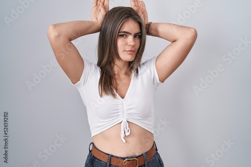 Young beautiful woman wearing casual white t shirt doing bunny ears gesture with hands palms looking cynical and skeptical. easter rabbit concept. photo